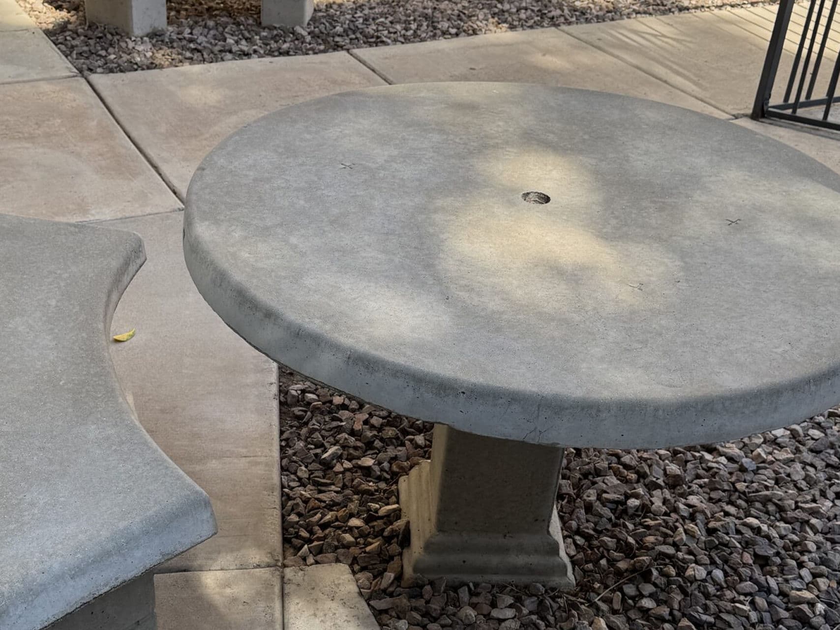 Concrete round table in a landscaped outdoor patio with gravel flooring.