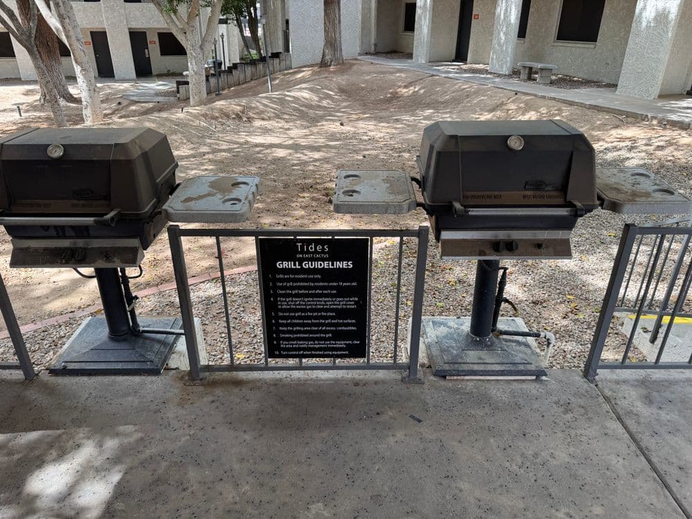 Two charcoal grills with a sign detailing grill guidelines at Tides residential area.